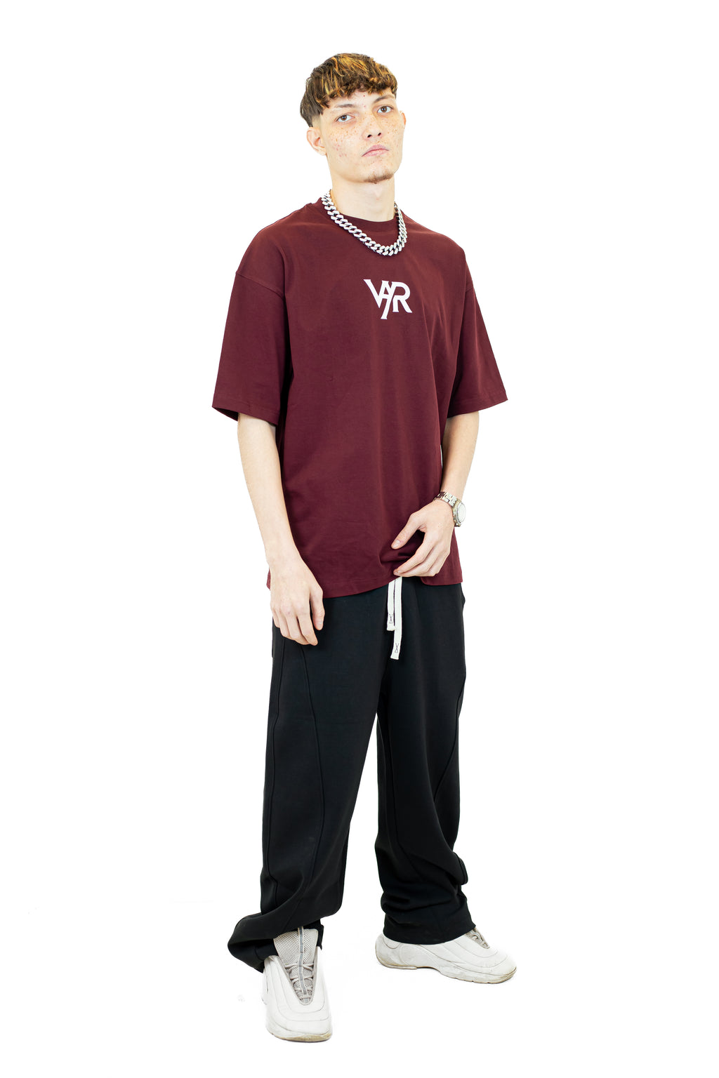 Person wearing a burgundy t-shirt with a logo and black pants on a white background